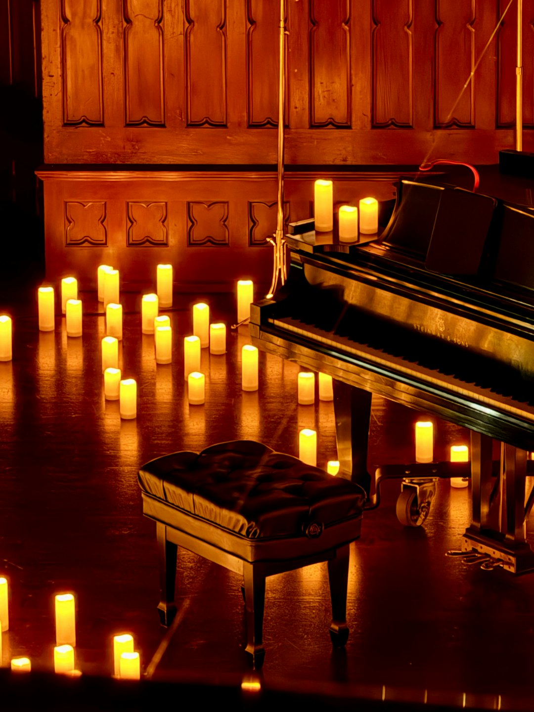 A grand piano surrounded by glowing candles on a wooden floor.